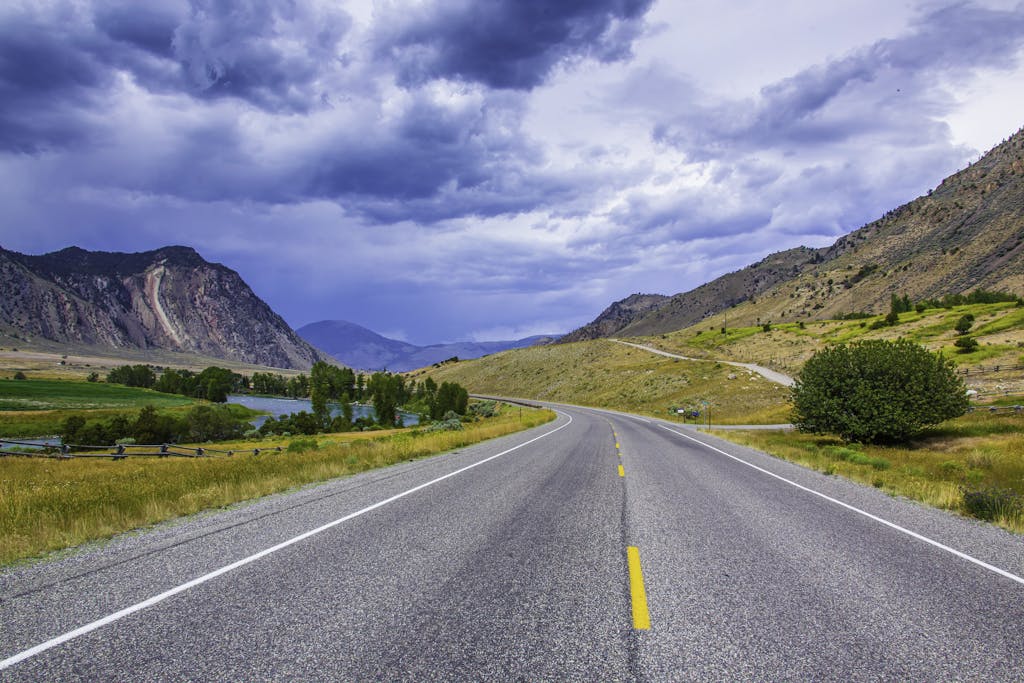 Explore the scenic mountain highway in Montana with vibrant natural beauty under dramatic skies.
